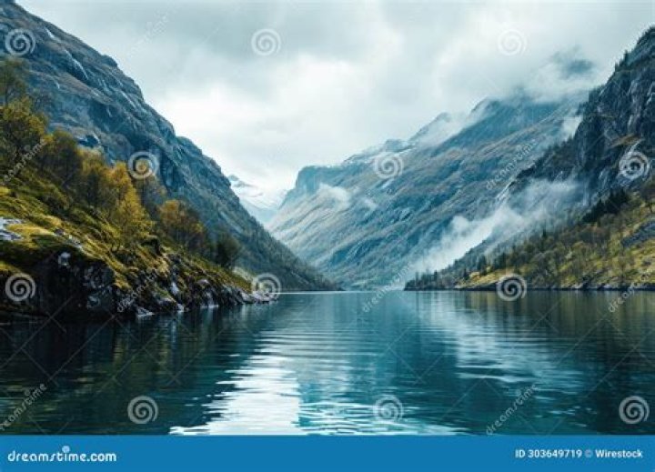 mountains surrounded by water under colorful sky at dusk with bright lights from buildings