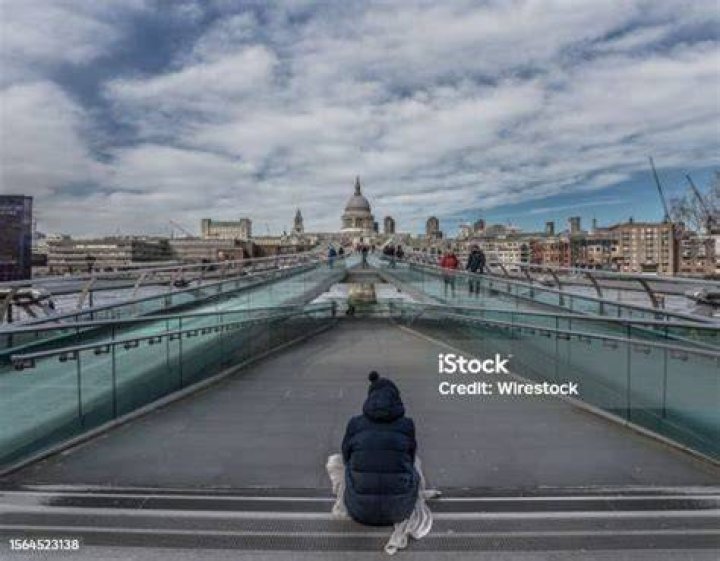 person sitting on bridge looking at water surrounded by buildings