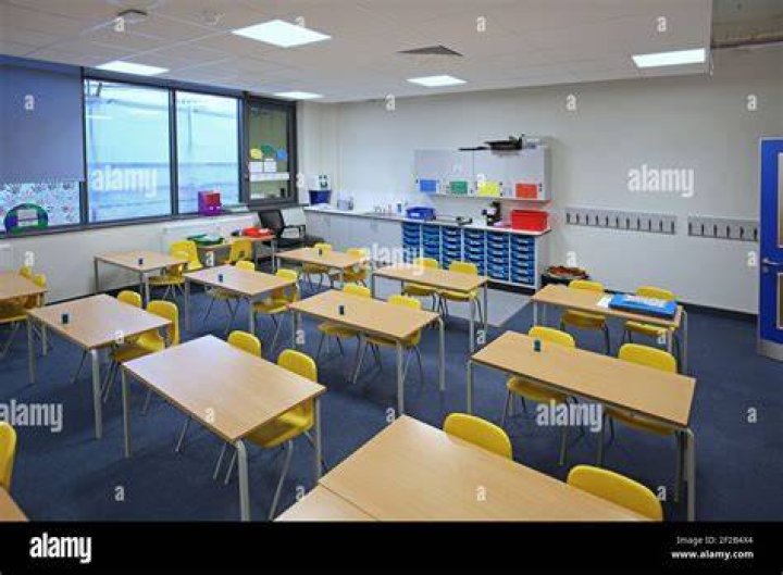 two rows of desks and chairs with desk and green chalkboard at the front of a classroom